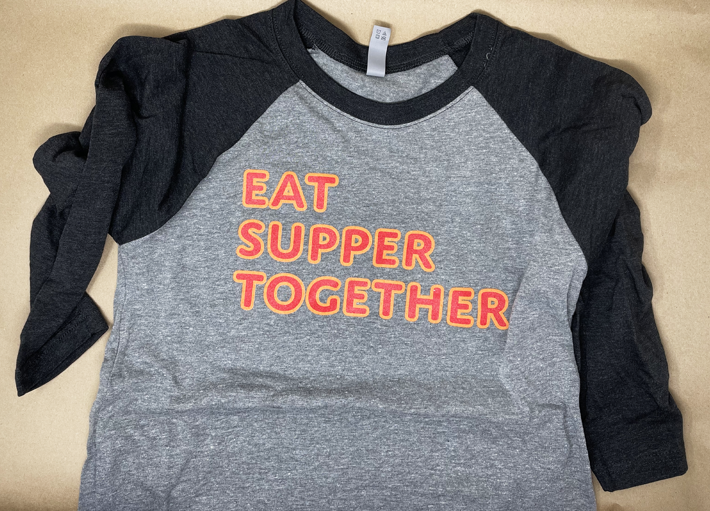Soft, comfortable gray and black baseball jersey style T shirt with 3/4 length sleeves. Text on front reads "EAT SUPPER TOGETHER"